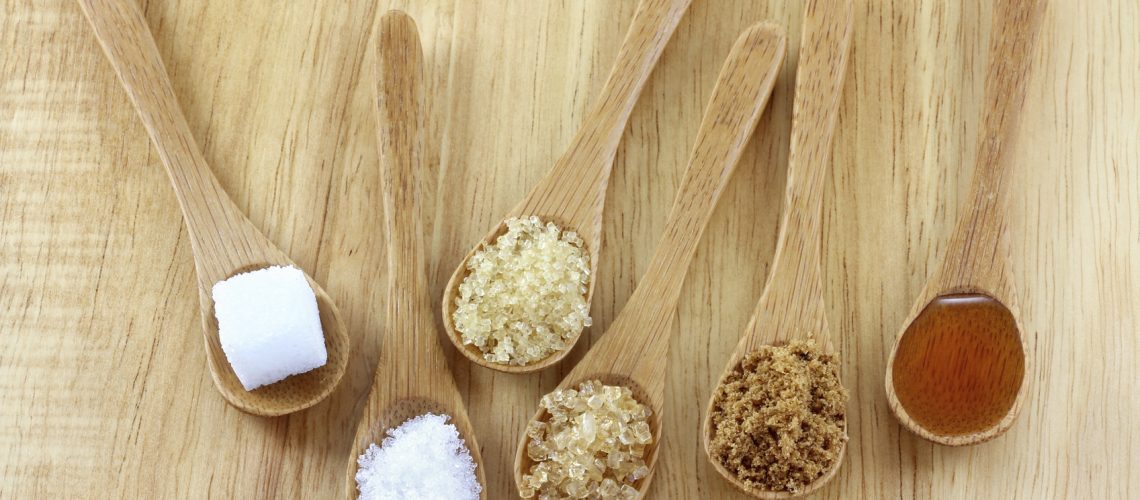Spoons of different types of sugar on the wooden background