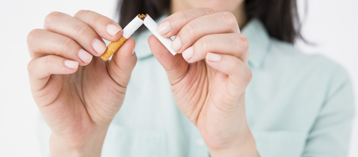 Smiling woman snapping cigarette in half on white background