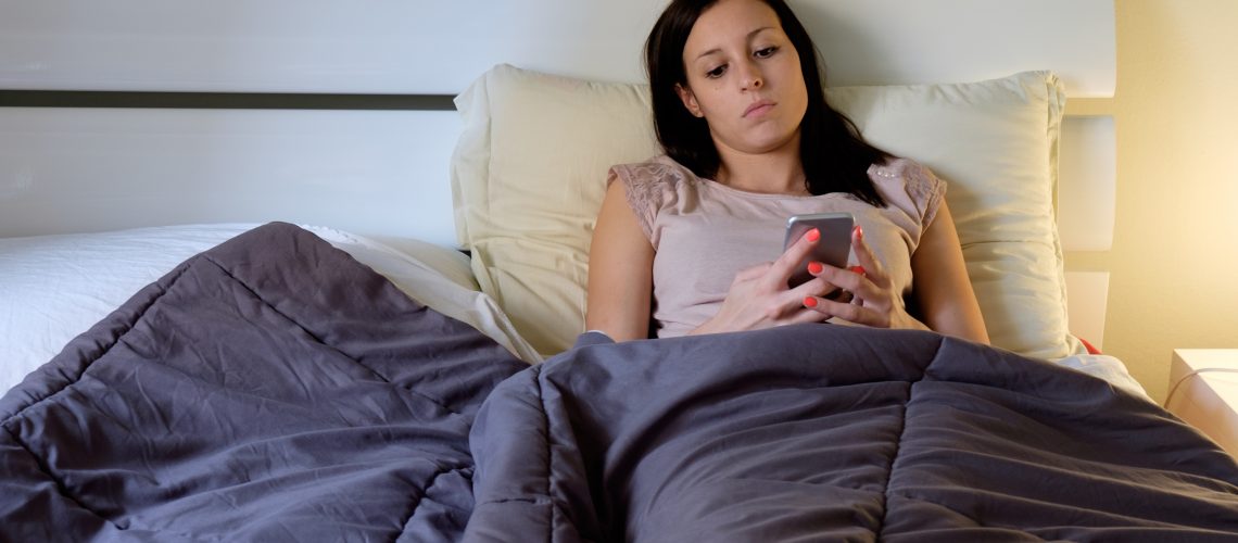 Young woman in bed and using her smartphone